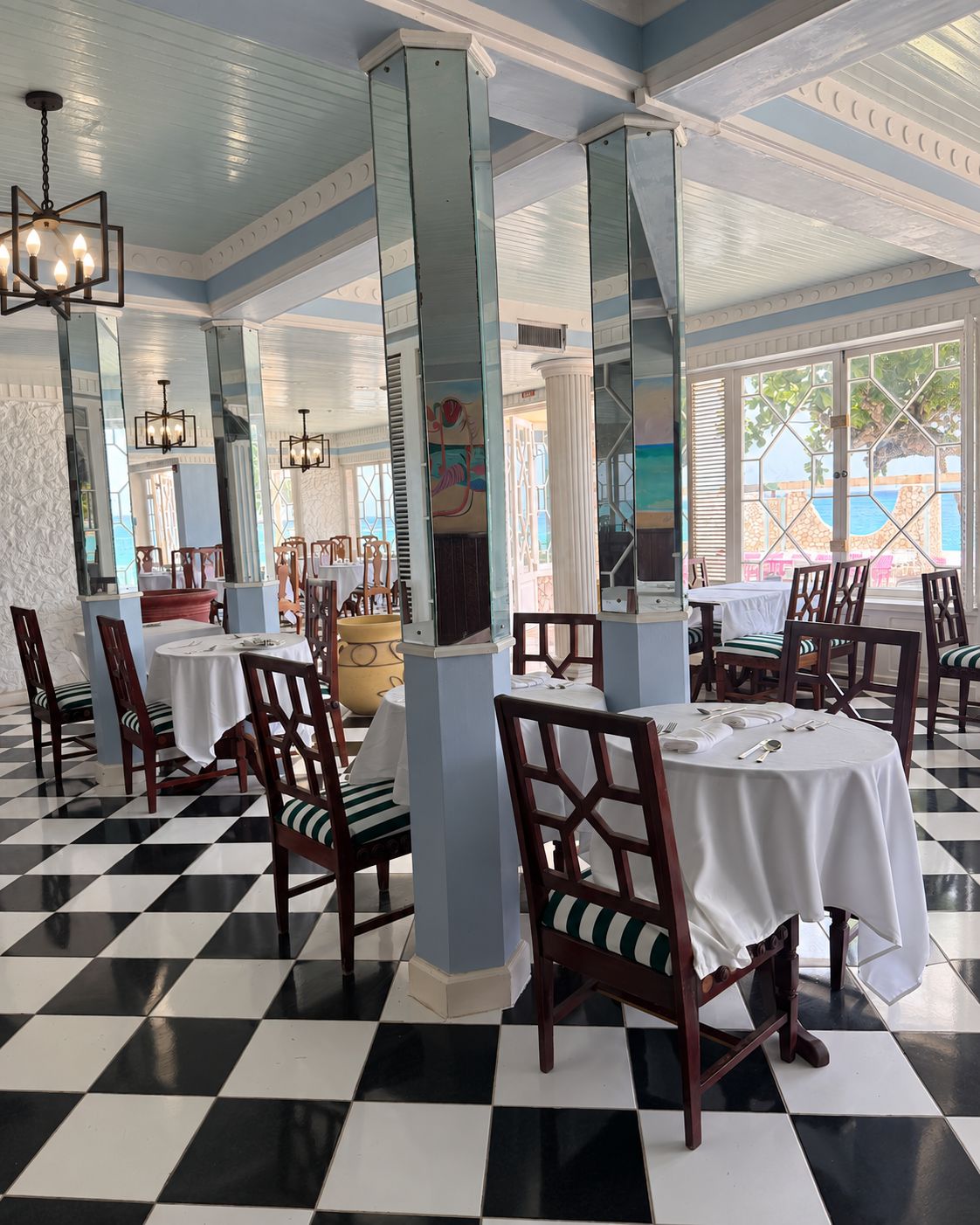 A dining area with checkered flooring, white tablecloths, and wooden chairs.