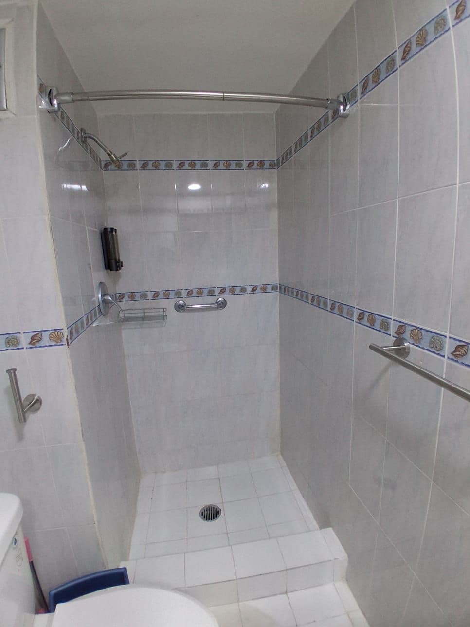A small, tiled bathroom with a shower, toilet, and a towel rack.