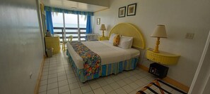 A hotel room with a bed, two bedside lamps, a window with curtains, a small table, and a chair. -  Sunny Beach Inn (Ocho Rios)