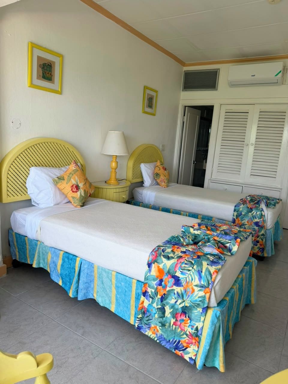 Una habitación con dos camas, cada una con cubrecama floral, cabecero amarillo y lámpara de noche.