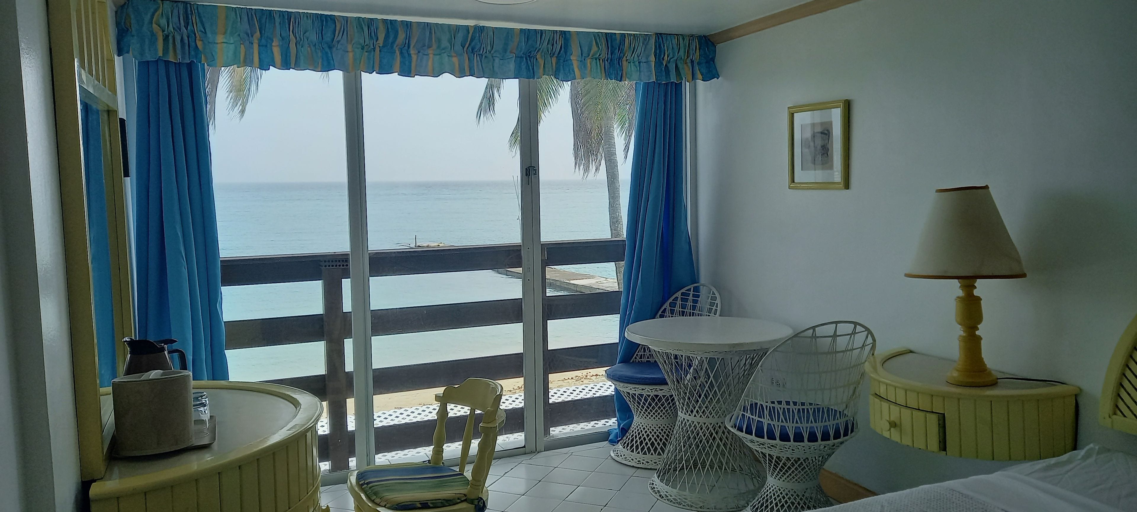 A room with a balcony, a bed, a chair, a table, and a lamp.