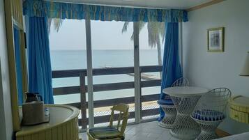 A room with a balcony, a bed, a chair, a table, and a lamp.