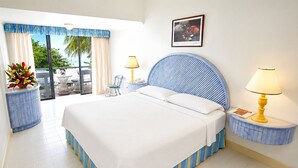 A hotel room with a bed, two bedside tables with lamps, a chair, a small table with a vase of flowers, and a view of the outdoors. - Sunny Beach Inn (Ocho Rios)