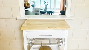 A kitchen area with a wooden countertop, a white cabinet with a wire rack, and a tiled floor. - Bright and Cozy London Apartment (London)