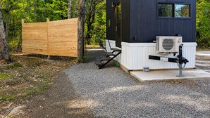 A modern cabin with a black exterior, a wooden deck, and an air conditioning unit.