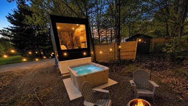 A hot tub with two chairs and a fire pit in a wooded area.