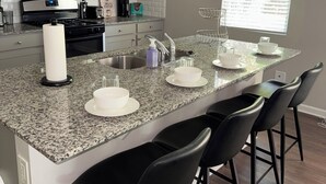 Una cocina moderna con encimeras de granito, electrodomésticos de acero inoxidable y taburetes de bar negros.