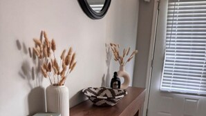 Un banco de madera con un florero y libros, un espejo en la pared y una puerta con persianas.