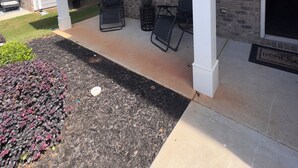 Un patio cubierto con mobiliario exterior, un muro de ladrillo y una puerta que da a la casa.