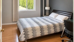 Un dormitorio con cama, mesita de noche, lámpara y ventana con cortinas.