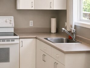 A kitchen with a built-in stove, a sink with a modern faucet, and a window with a view of greenery. - 1BR Suite on Forrester St – Cozy Victoria Stay (Victoria)