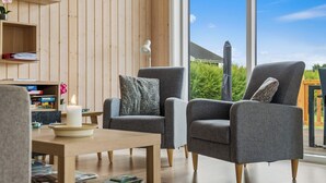 Ein modernes Wohnzimmer mit zwei grauen Sesseln, einem Holztisch und einem Bücherregal mit Büchern und Dekoration.