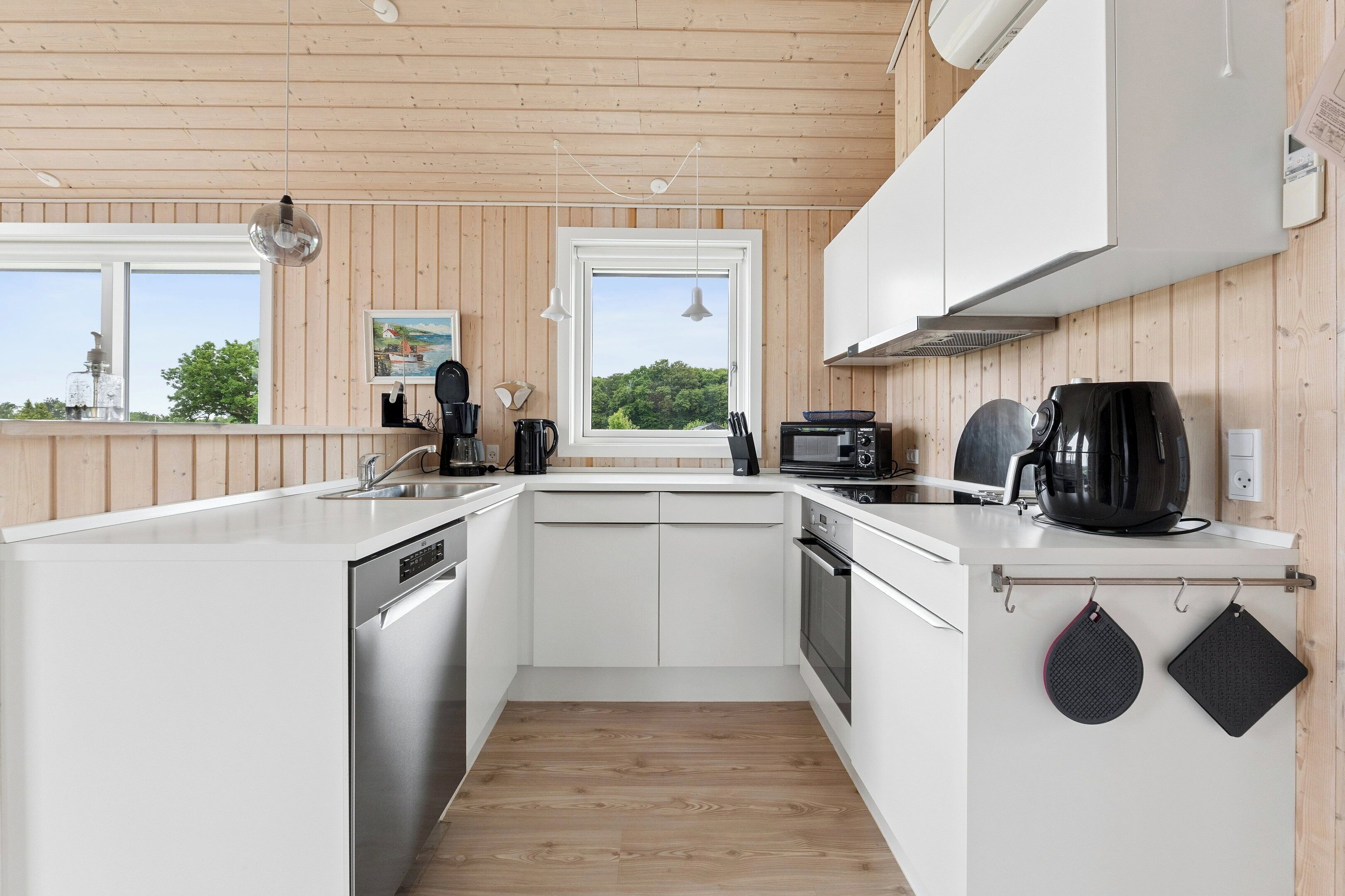 Ett modernt kök med vita köksskåp, diskmaskin, spis och mikrovågsugn.