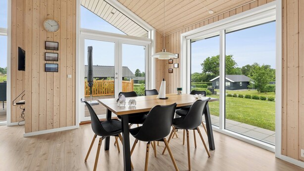 Ein stilvoller Essbereich mit einem Holztisch, schwarzen Stühlen und großen Fenstern mit Blick ins Freie.