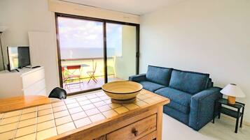 Una habitación moderna con una mesa de comedor de madera, un sofá azul, un televisor y un amplio ventanal con vistas a un balcón.