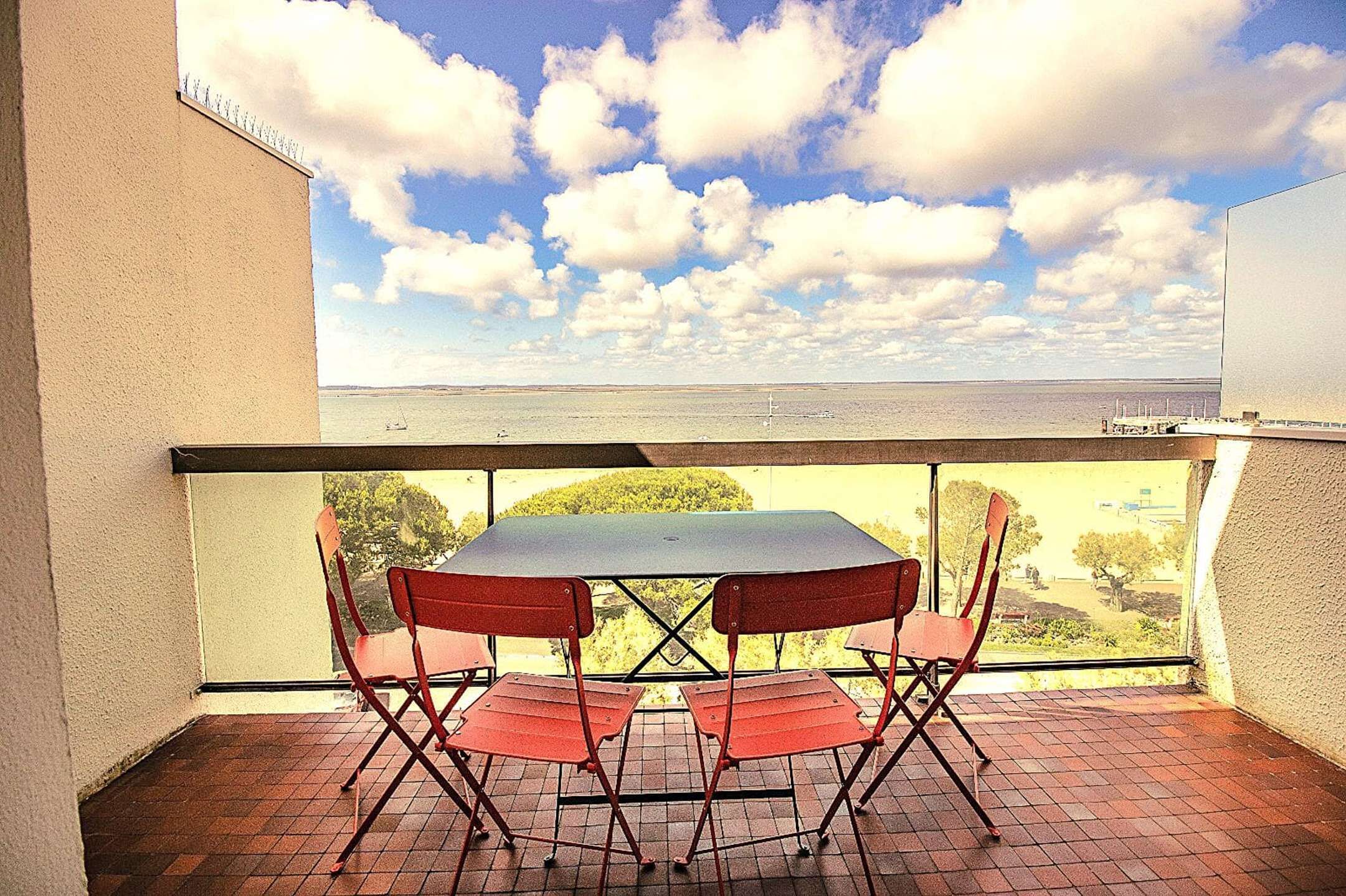 Un balcón con mesa y sillas, vista despejada al mar y cielo parcialmente nublado.