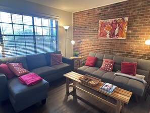 A living room with two sofas, a coffee table, a lamp, and a brick wall with a painting.