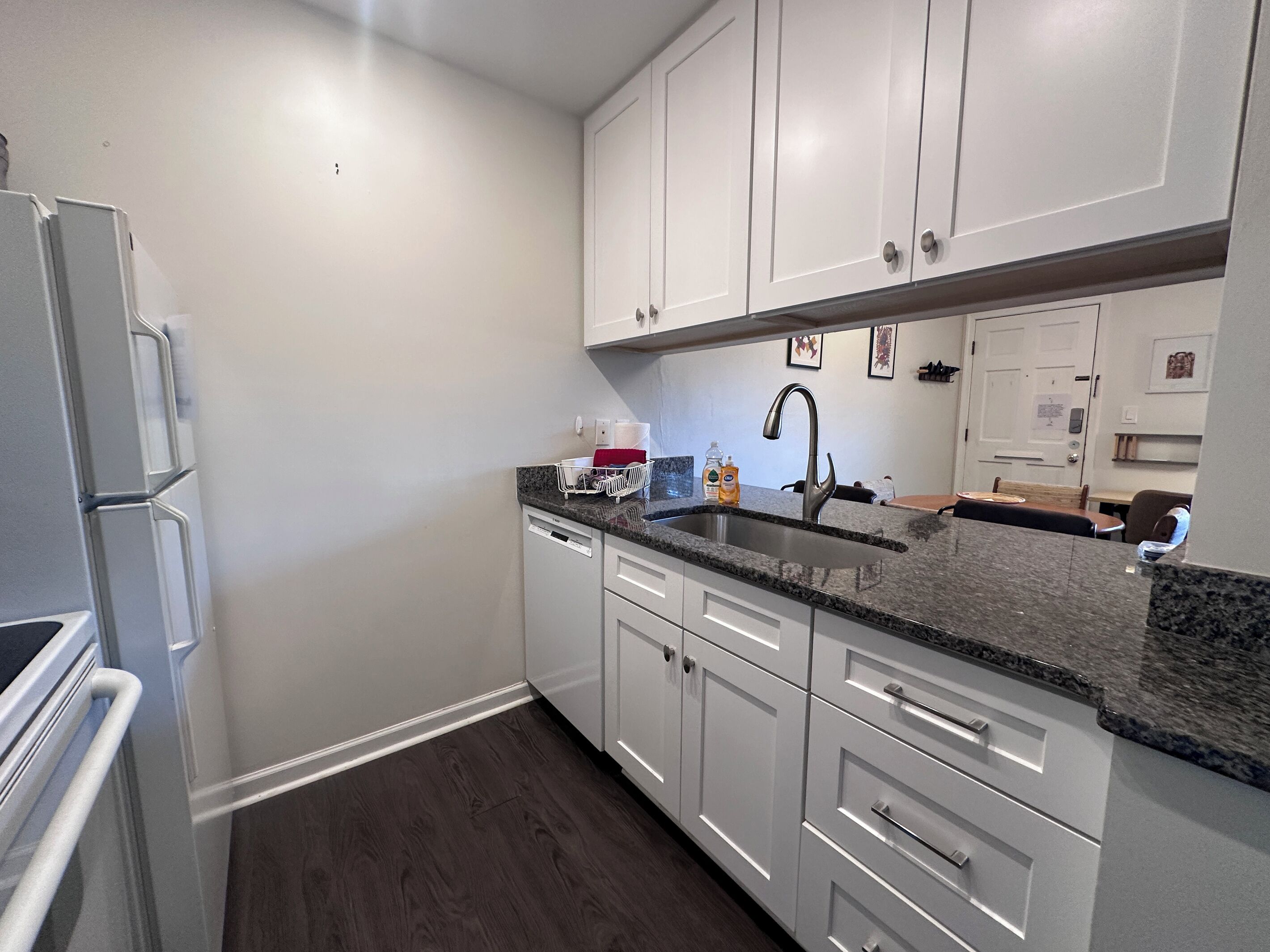 A kitchen with white cabinets, a granite countertop, a stainless steel sink, and a dishwasher.