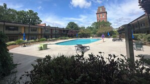 Un espace piscine avec des chaises longues, un bâtiment doté d’une tour et un ciel dégagé.