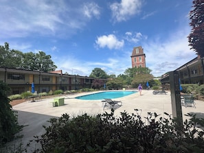 A pool area with lounge chairs, a building with a tower, and a clear sky.