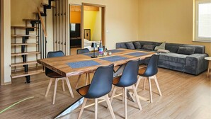 En moderne stue med et træspisebord, sorte stole, en grå sofa og en trappe med trægelænder.