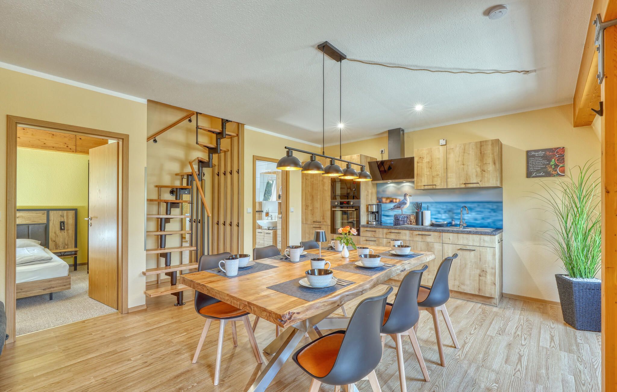 Une cuisine moderne avec des meubles en bois, un coin repas avec une table et des chaises en bois, et un escalier menant à une autre pièce.