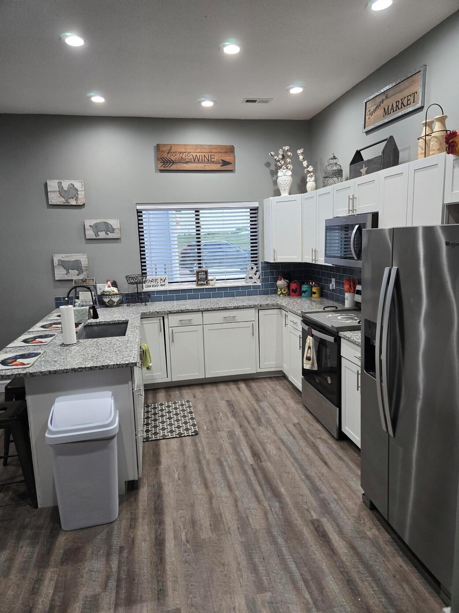 Una cocina moderna con armarios blancos, un refrigerador de acero inoxidable y una ventana con persianas.