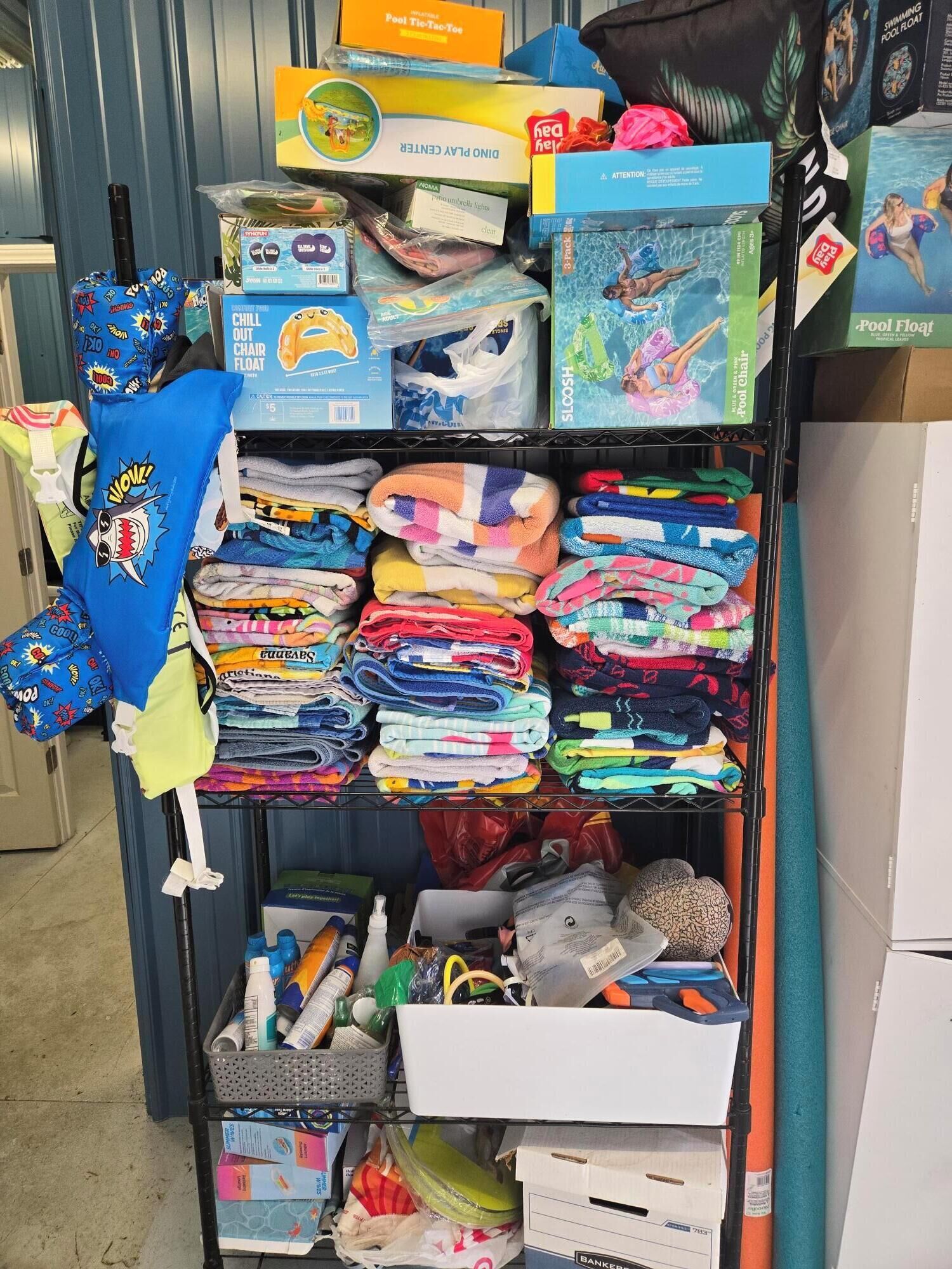 A shelf with various items including folded towels, pool floats, and a pool noodle.