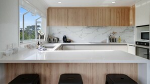 Een moderne keuken met een groot eiland, houten kastjes, een marmeren achterwand en uitzicht door het raam.
