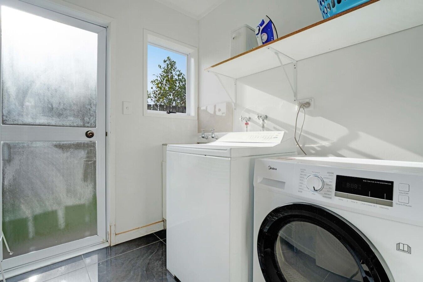 A laundry room with a washing machine, dryer, and a window with a view of a tree.