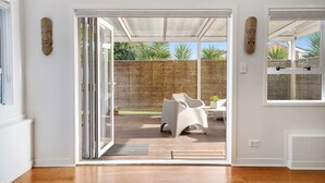 Een kamer met een schuifdeur die uitkomt op een terras met houten terras, wit meubilair en een bamboe hek.