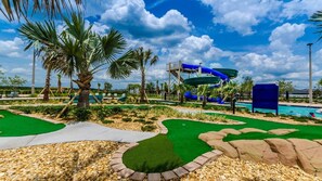 A water park with a large blue water slide, palm trees, and a pool area. - Whispering Palms - Eight Bedroom Villa, Sleeps 20 (Kissimmee)
