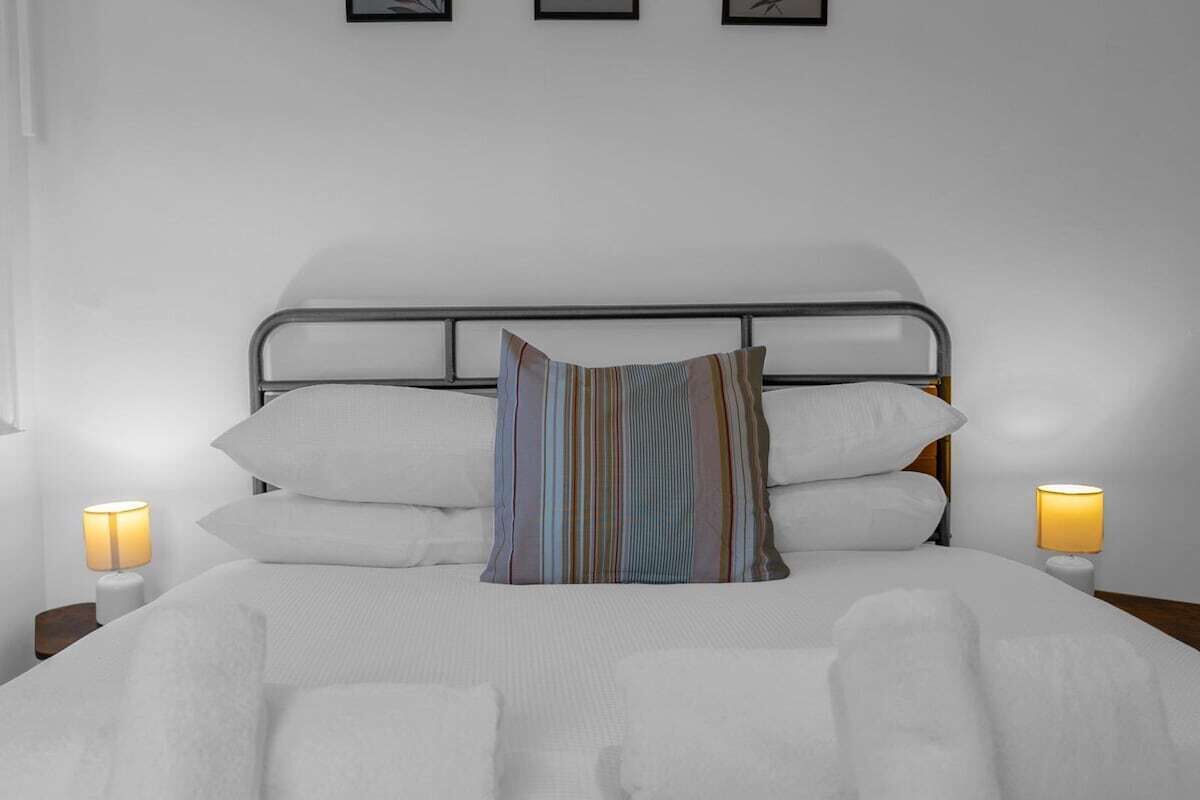 Un lit bien fait, avec du linge de lit blanc, une tête de lit en métal et deux lampes de chevet.
