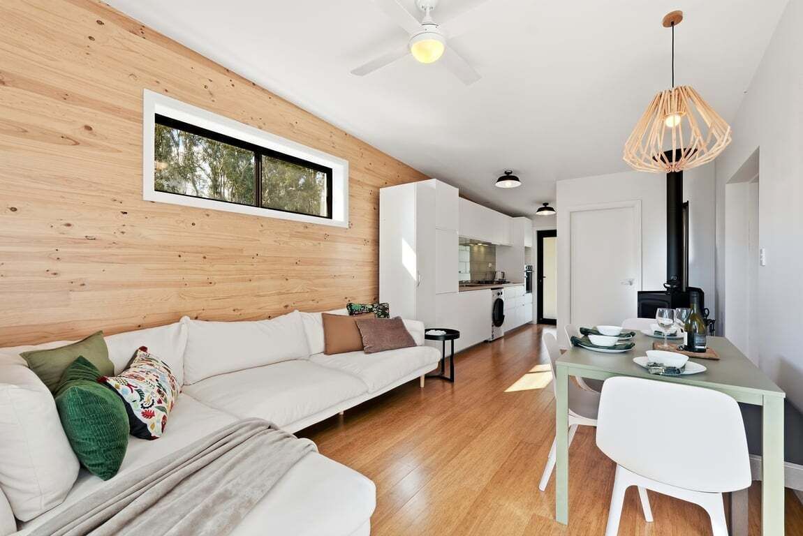 A modern interior with a wooden wall, a white sofa, a dining table with chairs, and a ceiling fan.