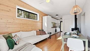 A modern interior with a wooden wall, a white sofa, a dining table with chairs, and a ceiling fan.
