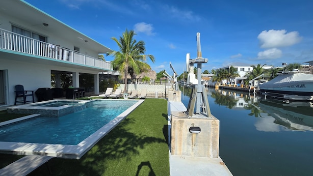 Ein Poolbereich mit einem Boot namens 'Whale Shark' in der Nähe, ein Gebäude mit einem Balkon und Palmen.