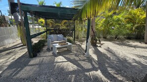 A covered outdoor seating area with a white bench and a table, surrounded by gravel and palm trees. - Canal front. Ocean access via Tavernier Creek. New pool and hot tub. Sleeps 8 (Tavernier)