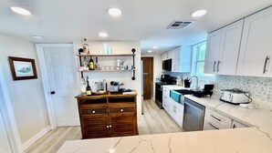 Eine moderne Küche mit weißen Schränken, einer Marmorarbeitsplatte und einem Holzschrank mit Flaschen.