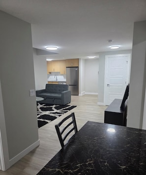A modern kitchen with a refrigerator, a dining area with a marble table, and a grey sofa. - Modern 2BR Suite | King Bed | Private Entrance I Glacier Ridge NW Calgary (Calgary)