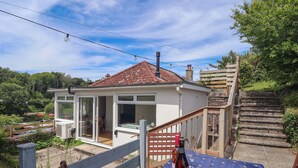 A house with a covered patio, a wooden staircase, and a table with a tablecloth. - Walnut Major (Kingsbridge)