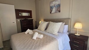 Un lit bien fait, avec des oreillers et des serviettes enroulées, une commode avec des tiroirs, une lampe et un tableau accroché au mur.
