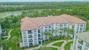 A multi-story hotel with a red-tiled roof, surrounded by lush greenery and a river in the background. - Spacious 3BR VistaCay Condo Near Disney, Universal & Orlando Attractions with Resort Amenities (Orlando)