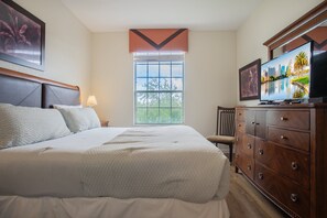 Ein Hotelzimmer mit einem großen Bett, einem Fernseher, einem Schminktisch und einem Fenster mit Blick auf Bäume.
