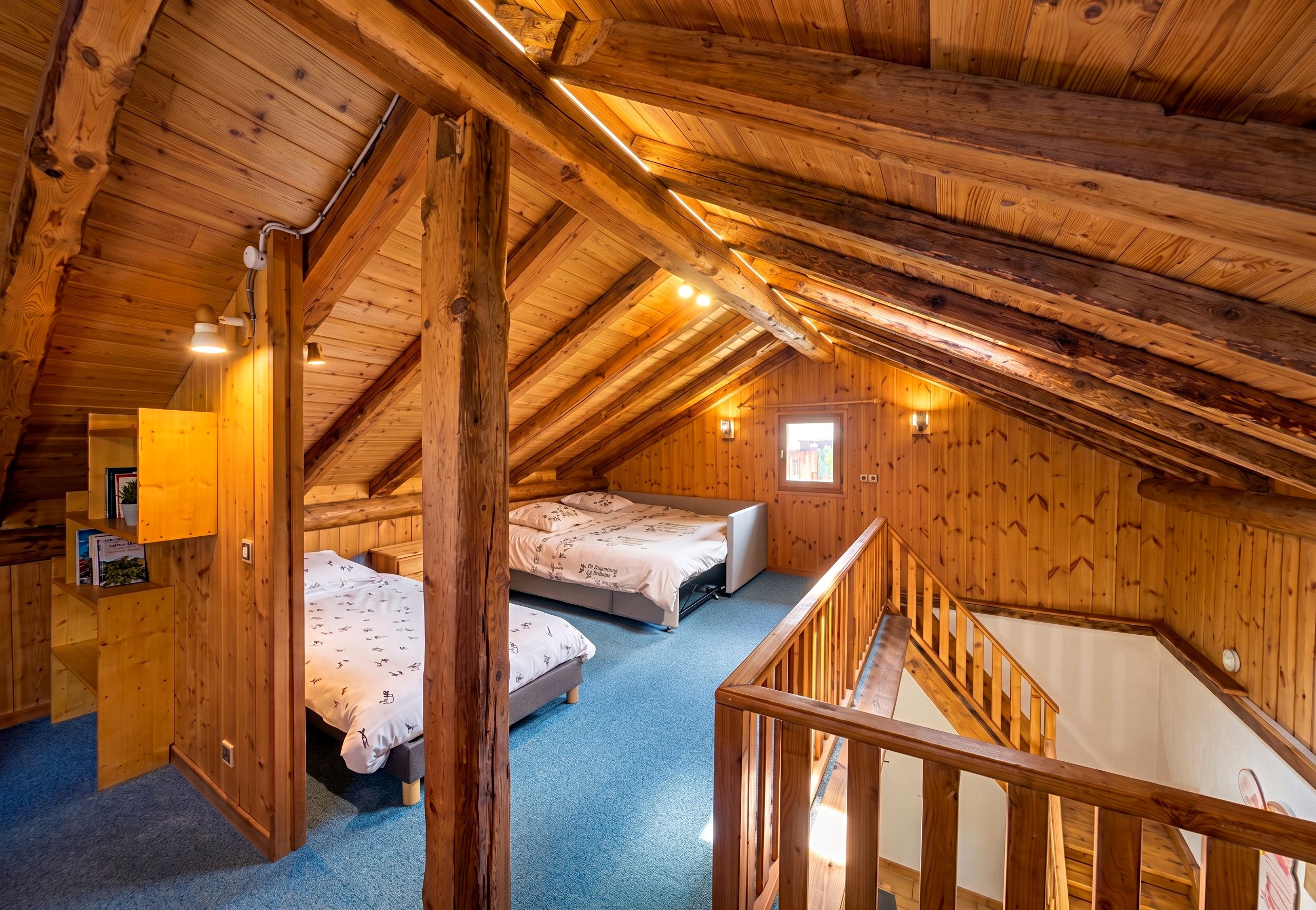 Una camera da letto mansardata in legno con due letti, una piccola finestra e una scala in legno.