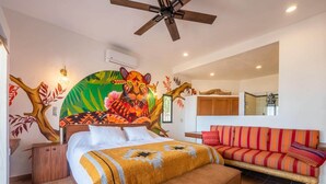 Une chambre à coucher comprenant un lit, un banc, un canapé, un ventilateur de plafond et une fresque murale.
