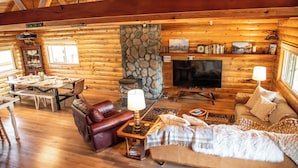 L’intérieur d’une cabane en rondins, avec une cheminée en pierre, des meubles en bois et un téléviseur.