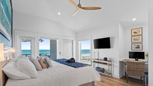A bedroom with a bed, a desk, a chair, a TV, and a view of the ocean. - Fall Deals + Snowbird Rates | Gulf Front Beach Escape (St. George Island)