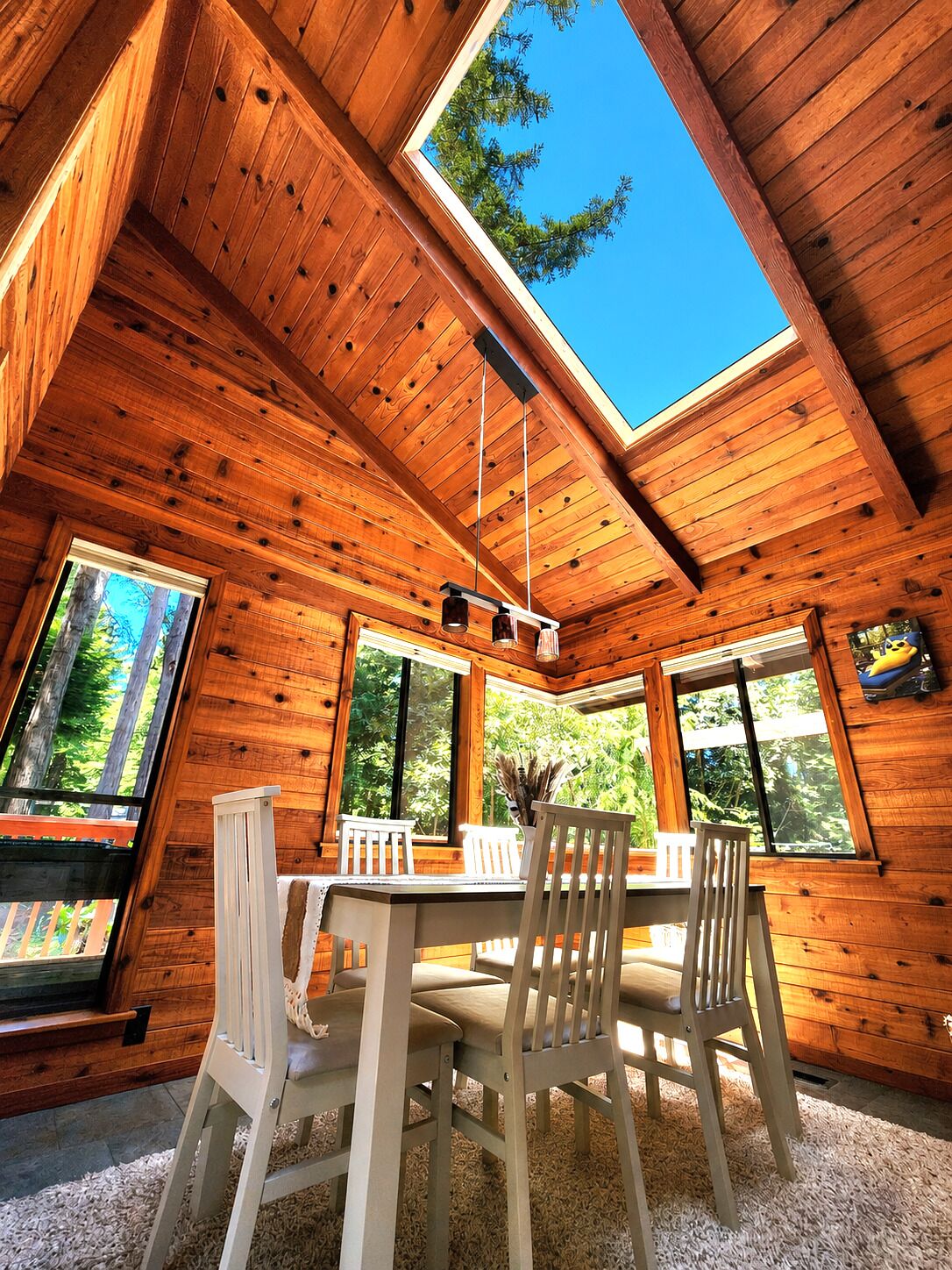 Une cabane en bois avec un coin repas, de grandes fenêtres et une lucarne.