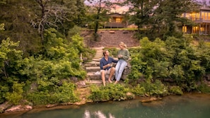 Un couple est assis sur des marches de pierre, surplombant un étang, entouré d’une végétation luxuriante et d’une terrasse en bois.