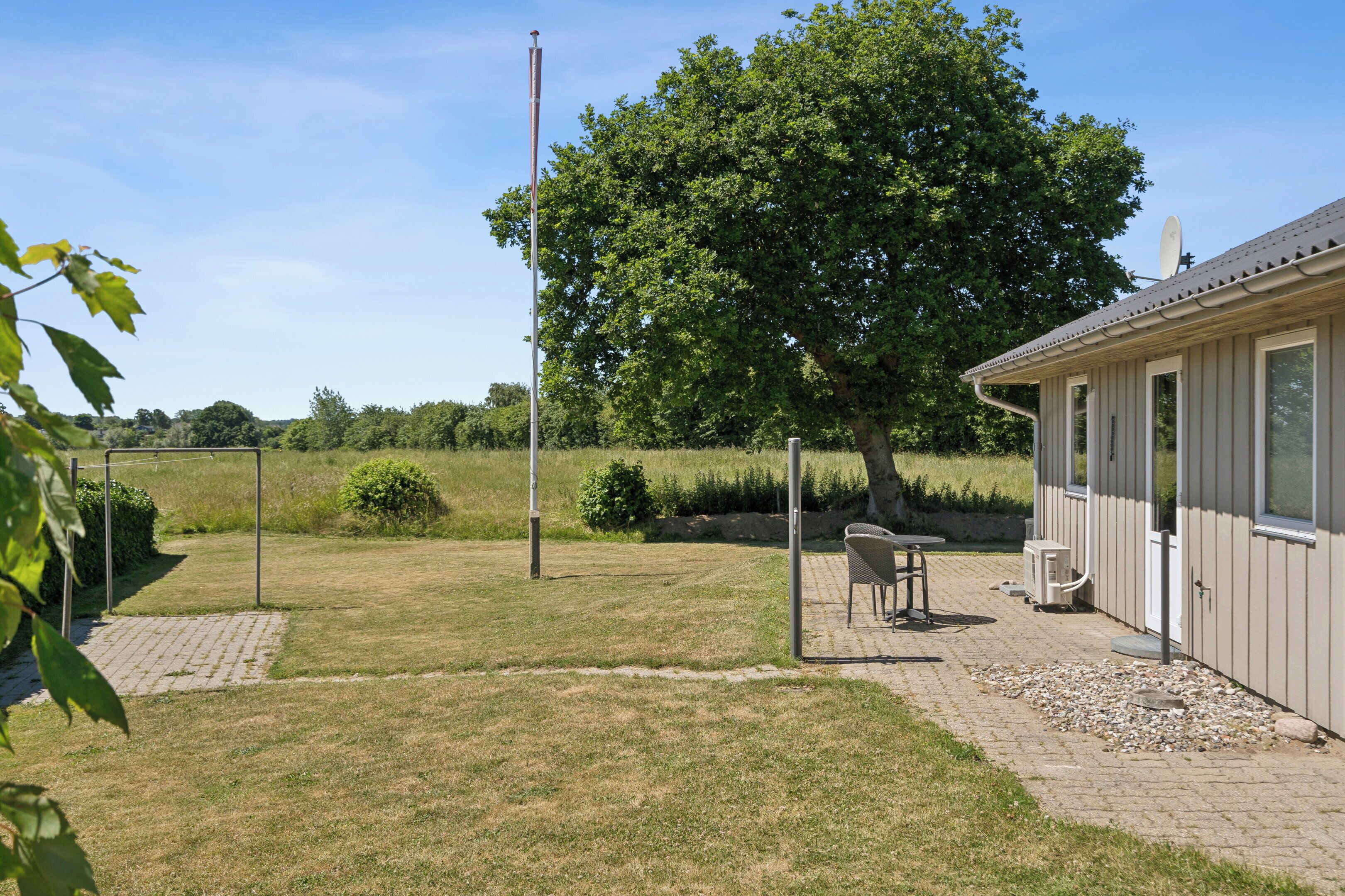 Il s'agit d'une propriété résidentielle dotée d'une terrasse dallée, d'une pelouse, d'un grand arbre et d'une antenne parabolique.